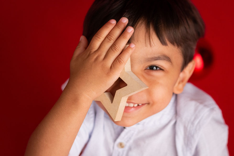 Child smiling, holding star-shaped object over eye.