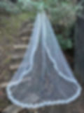 Lace-trimmed wedding veil draped over wooden steps in a forest setting, surrounded by greenery. Peaceful, natural ambiance. READING BRIDAL DISTRICT. CINCINNATI, OHIO. BOCHIC BRIDAL BOUTIQUE. ERICA KOESLER. WEDDING VEIL DESIGNERS.
