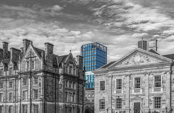 Black and white fine art architectural photography in Dublin with selective color, showing the historic stone facades of Trinity College and a modern blue glass skyscraper rising in the background. Massimo Cicconi Photography.