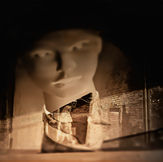 Double exposure on film: a mannequin's face and a female silhouette in motion. An experimental photographic work in warm tones that uses the transparency of the negatives to represent layered memory.
