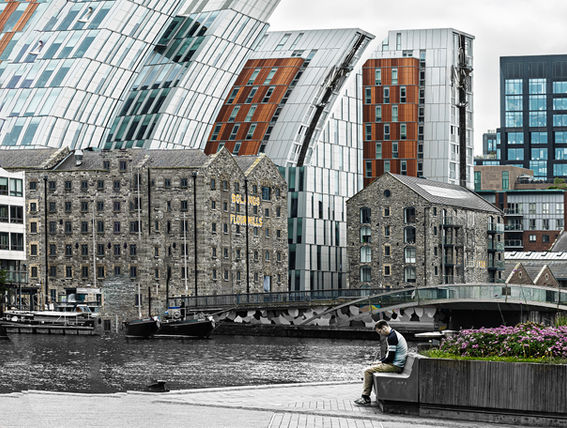 Fine art urban photography in Dublin, featuring the contrast between the historic stone buildings of Bolands Mills and the modern geometric architecture along the canal, with a lone observer sitting in the foreground. Massimo Cicconi Photography.