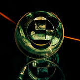 Fragments of analog negatives arranged in a cross shape and enclosed within a circular optical structure. The image, characterized by a specular reflection and a diagonal beam of light, explores the recomposition of reality through transparency and optics.