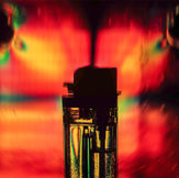 Digital chromatic abstraction with a dynamic radial effect. Warm red and yellow tones contrast with iridescent highlights in a symmetrical composition that explores the refraction of light through polarizing filters.