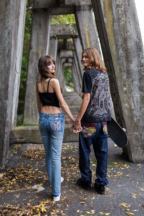 young couple in jeans are holding hands and smiling, looking backward
