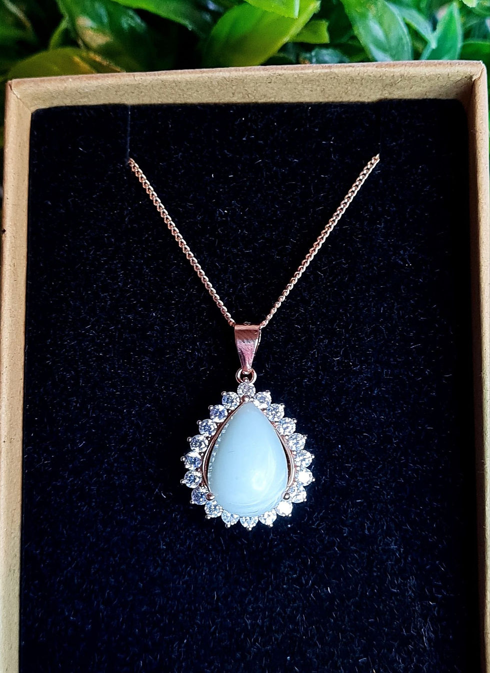 Thumbnail: Teardrop breastmilk necklace with 14x10mm stone and crystal halo setting, shown in rose gold on black display box.