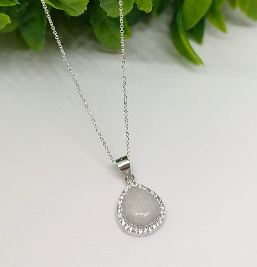 Thumbnail: Dainty breastmilk necklace in a crystal teardrop setting with 8x10mm stone on gold chain, shown with soft floral backdrop.