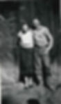 Eleanor and an unknown suitor smiling while standingside by side in front of a wooden structure. Eleanor wears a patterned top and skirt and dress shoes, the man wears a shirt and pants—probably a CCC uniform.