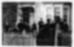 The Davis-Williams family stands in front of a white wooden house and picket fence. They are dressed in dark clothing, suggesting a serious or formal mood—likely the funeral of Thomas Olive Davis in 1886 at Sand Hollow, near Athena.