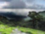 A distant rain storm visible from the side of a green hill