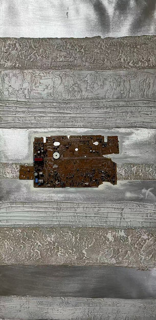 Narrow vertical mixed media work with horizontal banding in silvers, greys, and a central band of dark rust and earth tones. The surface has an industrial, archaeological quality — layered like sediment or stripped wall. Small dark forms punctuate the central band like embedded objects or fossils