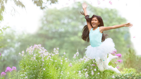 A girl jumps for joy surrounded by flowers in a garden