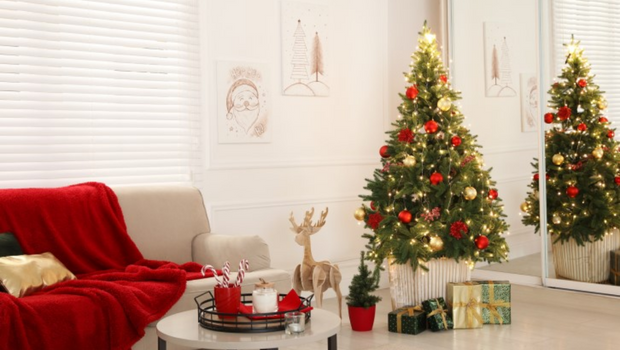 Decoração Natalina clean, com sofá branco e uma manta vermelha. Mesa de centro branca com pés pretos, sobre ela enfeites vermelhos. Arvore de Natal ao lado com enfeites dourados e aos pés dela presentes embrulhados