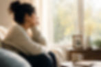 A thoughtful adult sits quietly beside a sunlit window in a cozy living room, gazing outside with a reflective expression. A framed family photo, coffee mug, and soft natural light create a warm, peaceful setting that symbolizes anticipatory grief, caregiving, and quiet contemplation.