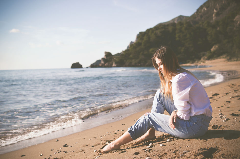 Young white woman sitting calmly on a sandy beach.