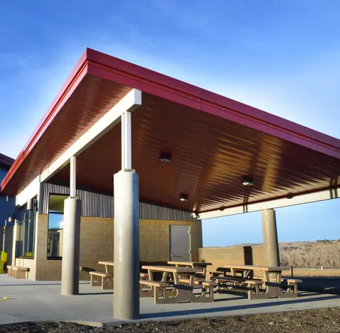 Open-air pavilion with red metal roofing, concrete columns, and picnic tables in Montana.