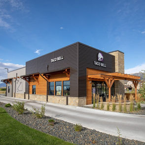 Modern Montana Taco Bell restaurant with dark metal siding, wood accents, and stone details 