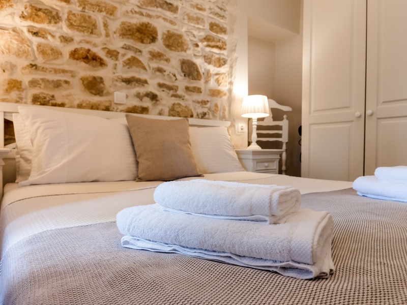 Bedroom with stone accent wall, double bed and folded towels at Spiti Mata Peritheia
