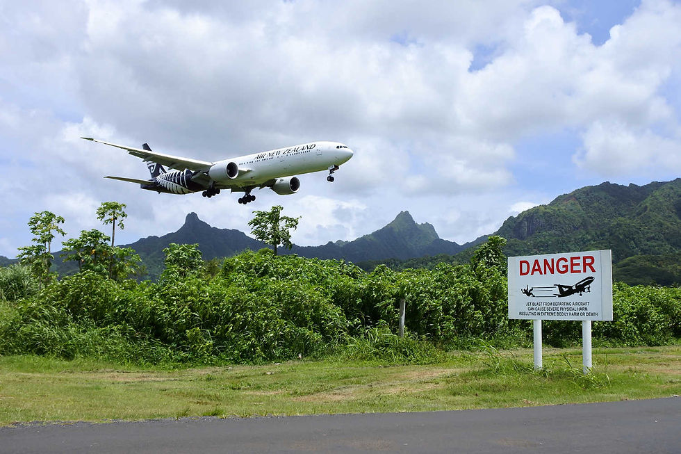 Air New Zealand plane landing at Rarotonga Airport beside a jet blast danger sign and green peaks