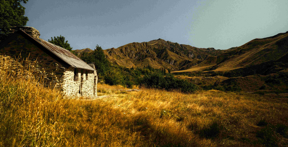 Macetown Needham's Cottage: The historic stone remains of Needham’s Cottage in the Macetown ghost town, surrounded by wild golden tussock grass and the rugged mountains of the Arrow River valley.