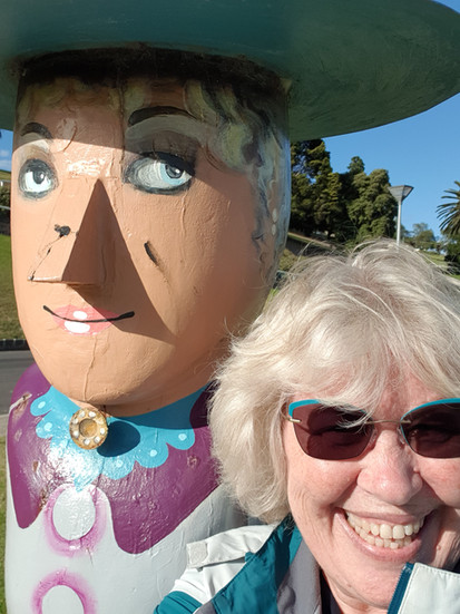 Smiling woman next to a large wooden sculpture in a hat
