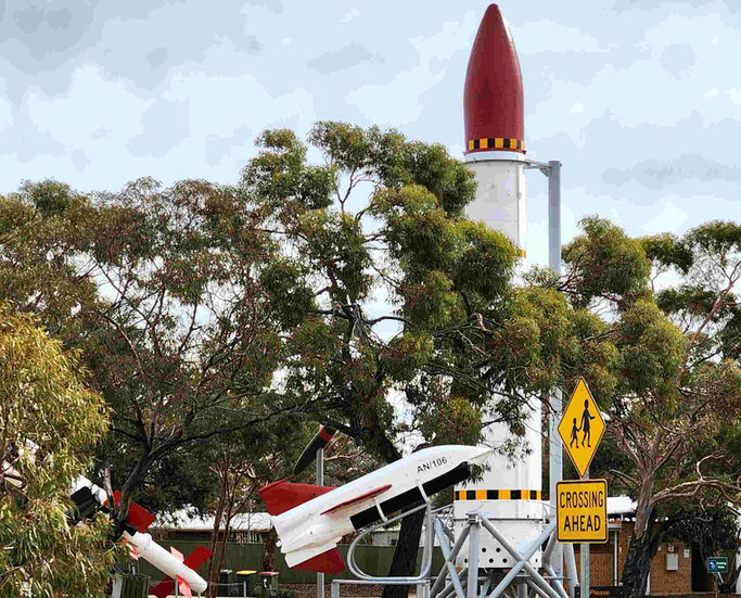 Large red and white rocket display with a smaller model rocket and 'Crossing Ahead' sign