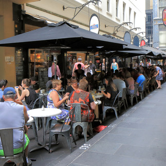 Melbourne Street Café: A vibrant outdoor dining scene in a Melbourne laneway, featuring patrons seated at small round tables under large black umbrellas alongside historic urban architecture.