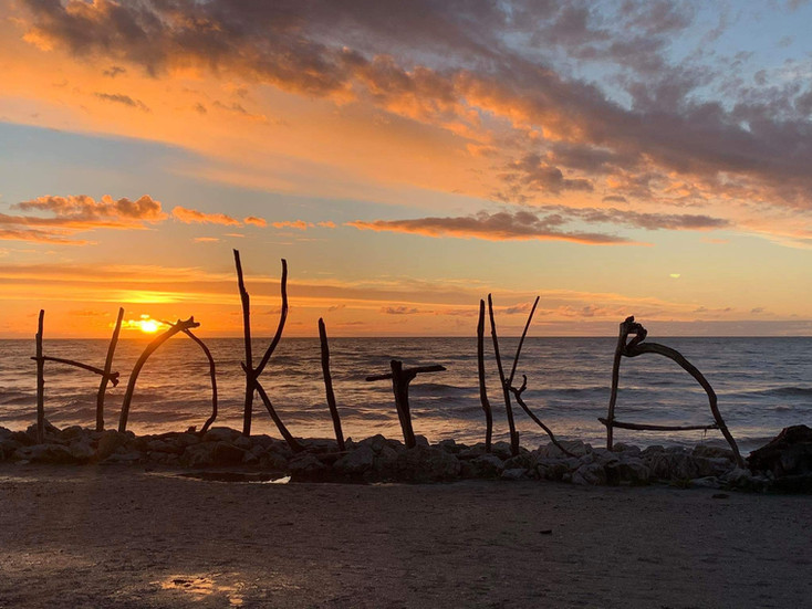 Sunset over ocean with driftwood letters spelling HOKITIKA