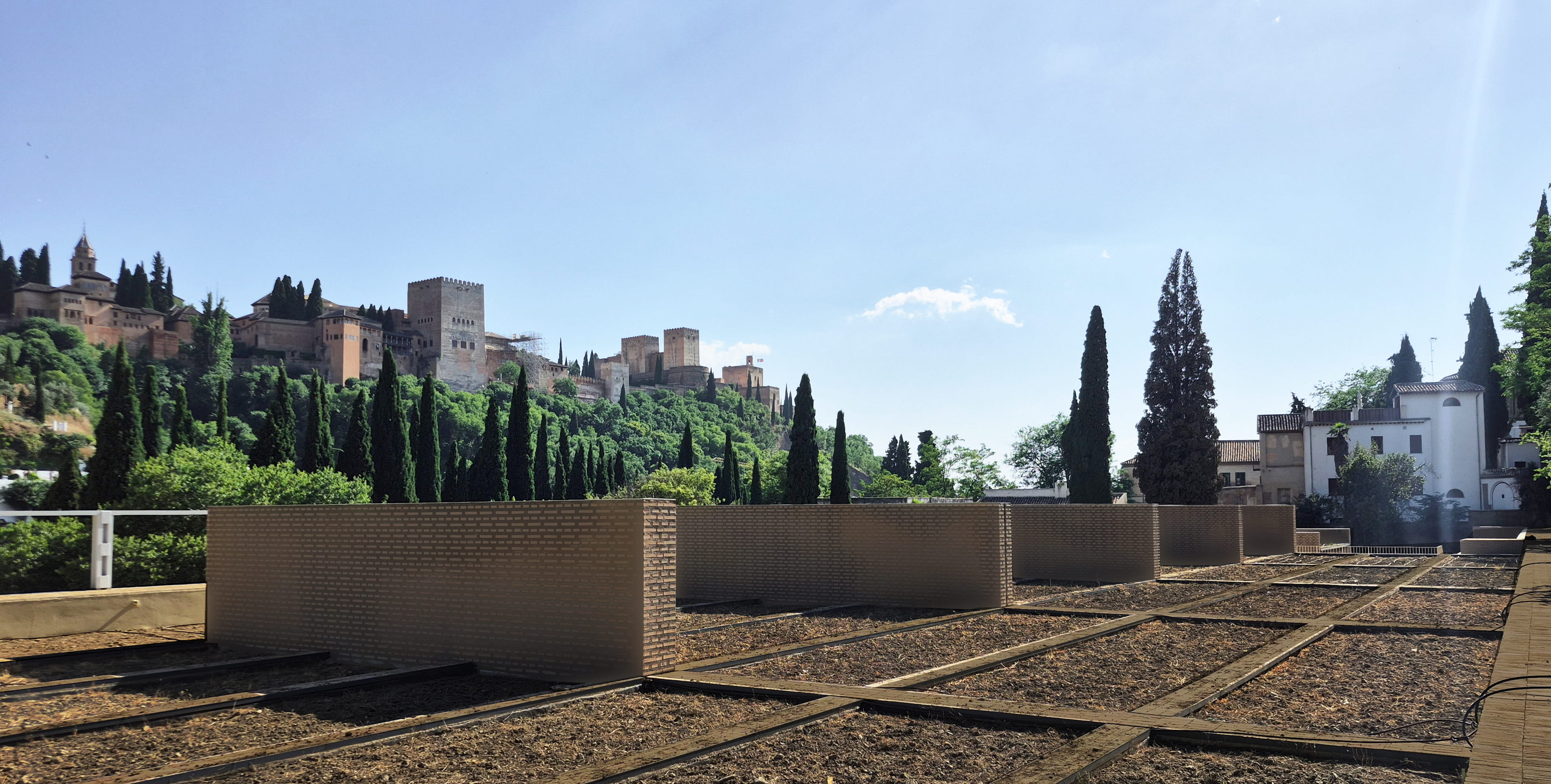 Panoramic view of the Alhambra palace complex in Granada, Spain, seen from the terraced roof garden of the Carmen del Negro archive. Modern structured brick walls and unplanted garden beds define the foreground terrace.