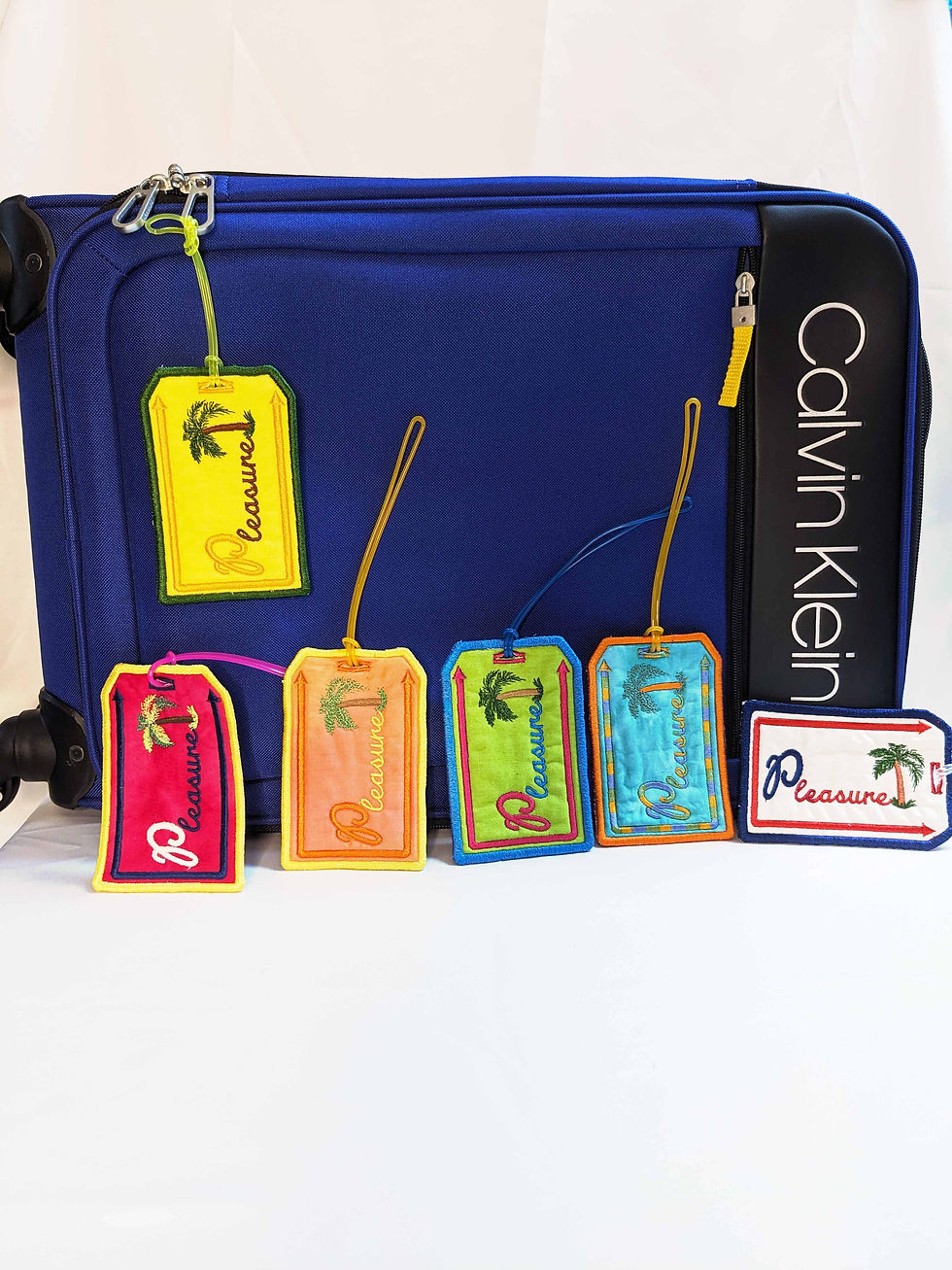 Embroidered Luggage tag with message "Pleasure" Main Background Color: White, Orange, Teal, Lime Green, Yellow, Fuschia, Fabric: 100 % Cotton, Vinyl, Size: 3 x 4-1/2", Special Features: Embroidered lettering, design and borders, vinyl on back for name card, Vinyl loop attachment to hook to luggage, JordynCherise