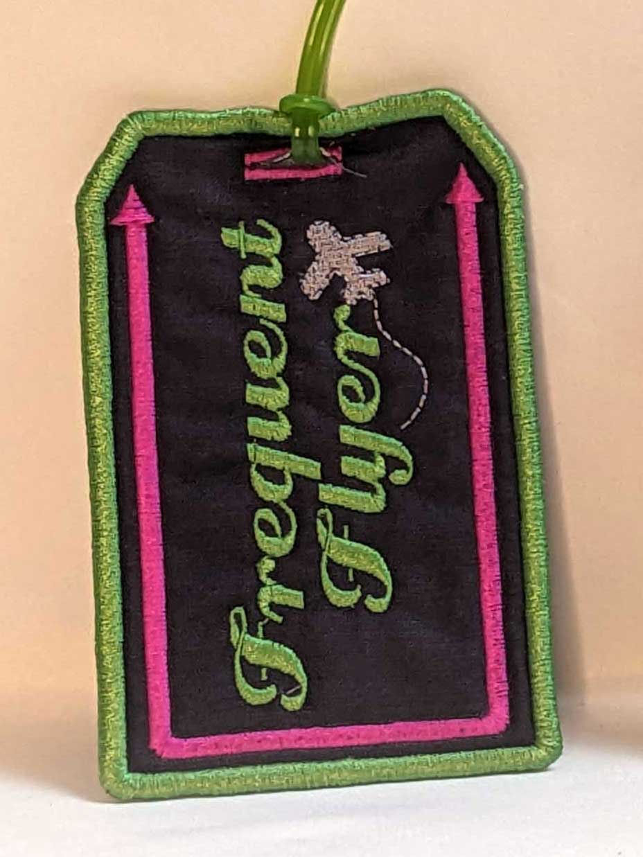 Thumbnail: Embroidered Luggage tag with message "Frequent Flyer" Main Background Color:  Dark Slate, Fabric: 100 % Cotton, Vinyl, Size: 3 x 4-1/2", Special Features: Embroidered lettering, design and borders, vinyl on back for name card, Vinyl loop attachment to hook to luggage, JordynCherise