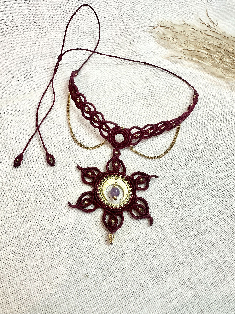 Collier en micro-macramé bordeaux Perséphone, avec lune en laiton, améthyste et fines chaînettes, posé sur un tissu clair.
