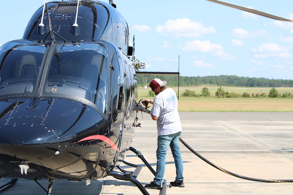 Ground crew refueling a black helicopter on a sunny day.