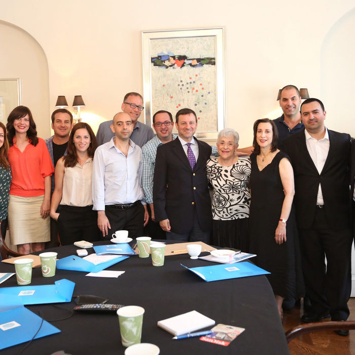 קבוצת אנשים מצולמת ליד שולחן עם תיקיות. משלחות העיתונאים וחברי כנסת. תמונה עם רקע משרדי.