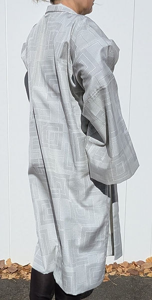 Plan complet d'un manteau Kimono moderne gris argenté et unisexe, avec texture tissée transparente mise en valeur par le soleil.