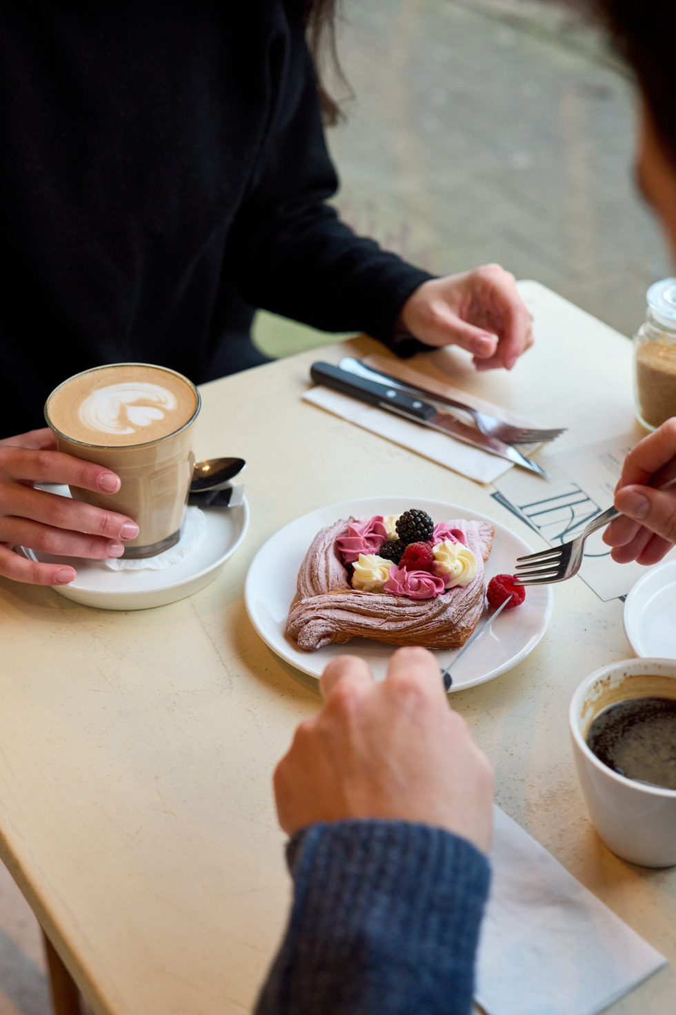 Latte and pastry on table with people dining.