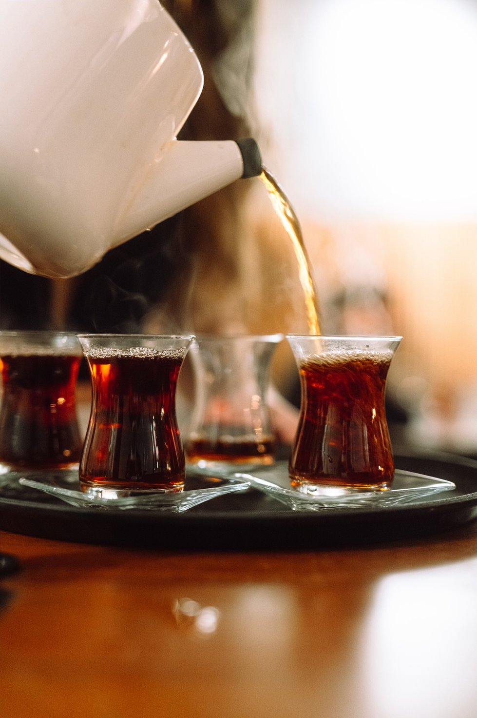 Teapot pouring tea into glasses on a tray.