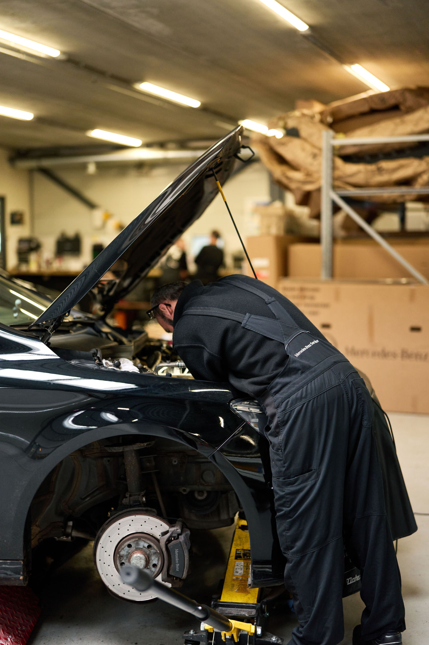 Mechanic working under car hood in garage.
