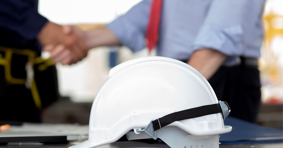 White hard hat on a table in front of a blurred handshake between two workers, one in a red tie, in an office setting