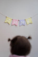 Jong kind dat kijkt naar een muur waar een wolvilten slinger van vlaggen hangt in diverse tinten met de naam 'JUNE'