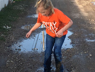 girl in orange shirt and jeans jumping in a mud puddle