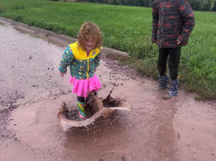 girl in rainbow rain boots pink skirt jumping in mud puddle