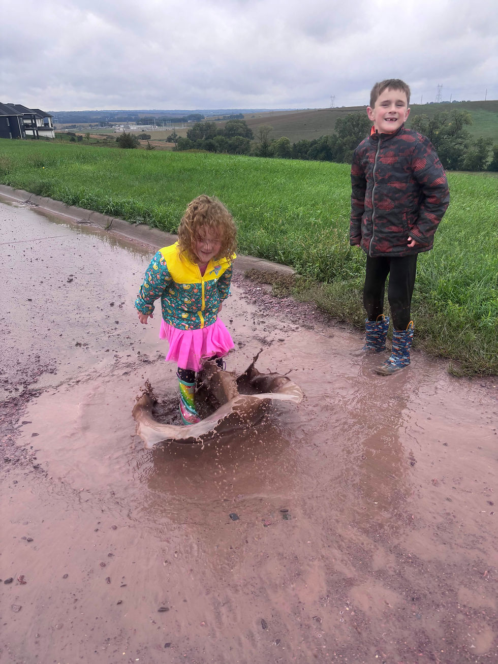 girl in rainbow rain boots pink skirt jumping in mud puddle
