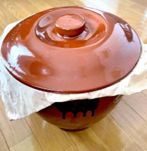 味噌づくりの途中で発酵中の味噌を、布をかぶせた茶色の味噌樽に入れて熟成している様子。