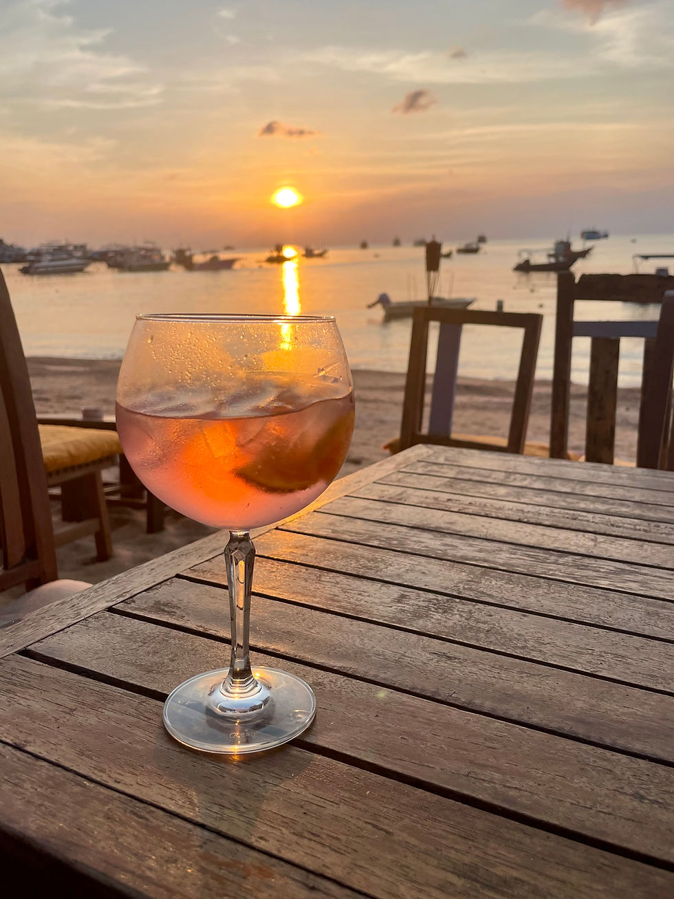 Sunset in Mae Haad, Koh Tao, Thailand with a single tropical drink on a wooden table — a calm evening scene popular with solo travelers.
