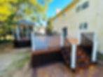 Spacious backyard featuring a new multi-level deck with illuminated stairs and railing, adjacent to a gazebo and a light-colored house.