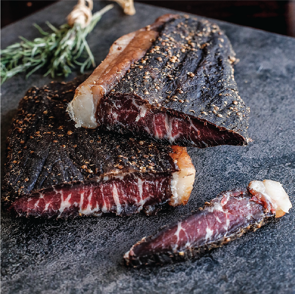 Slices of dry-aged, marbled meat on a dark stone surface. A sprig of rosemary rests nearby, creating a rustic, gourmet feel.