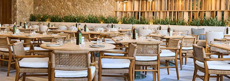 Empty upscale restaurant with wicker chairs and set tables, stone wall and greenery, calm warm ambiance.
