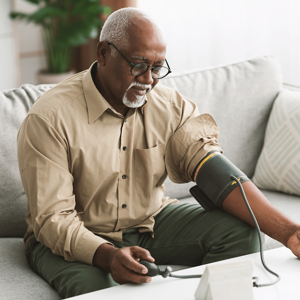 Elderly man in glasses checks blood pressure on a grey sofa, wearing a beige shirt. Calm expression, plants and soft lighting in background.