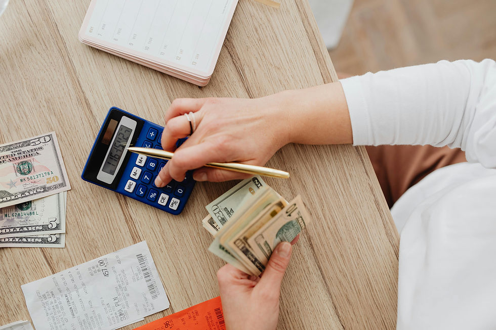 Hands using a blue calculator and holding cash on a wooden table with receipts. A notepad and money are visible, creating a budgeting scene.