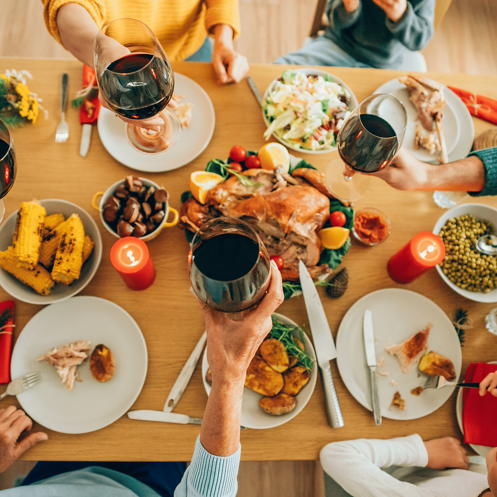 People toast with red wine over a festive dinner table with a roasted turkey, corn, and salads. Red candles add a warm, celebratory mood.